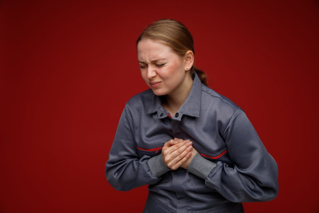 Person experiencing chest pain and clutching their chest, showing common heart attack symptoms such as chest pressure, pain radiating to the arm, and shortness of breath.