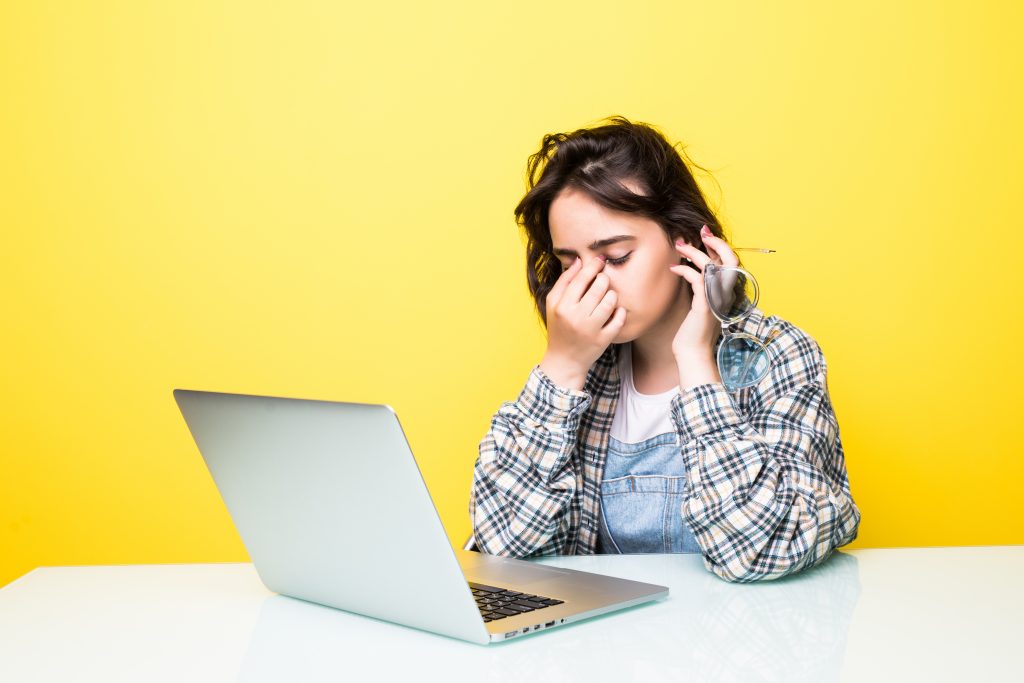 Person experiencing pain on the bridge of the nose while using a laptop due to digital eye strain, poor posture, or sinus pressure.